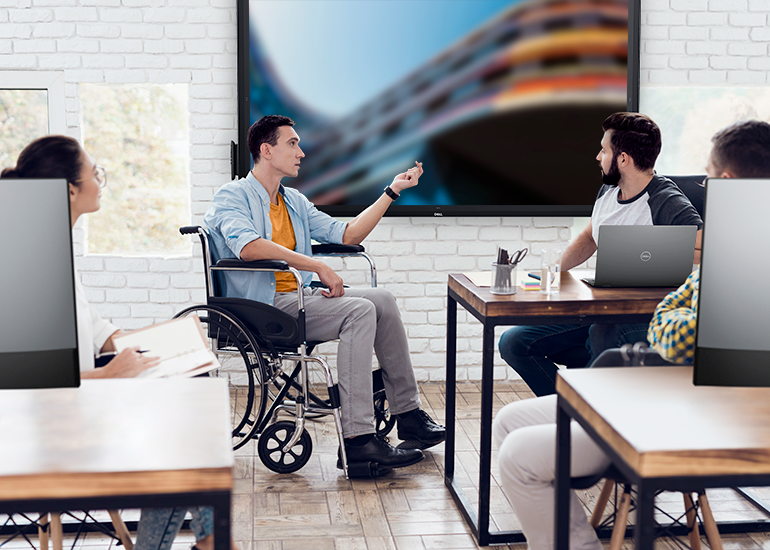 A man in a wheelchair in front of digital screen speaking to colleagues